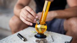 Man packing bong with joint on the table before he smokes weed
